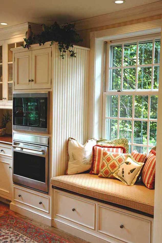 Comfortable window reading nook next to wall oven and cabinet area in traditional kitchen design.